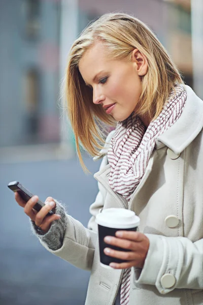 Connected to the city. an attractive young woman sending a text while drinking a coffee in the city streets