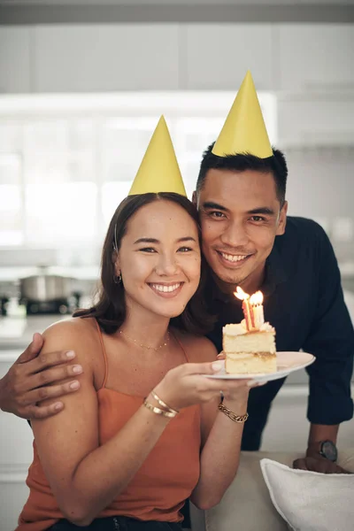 Portrait, birthday cake and smile with a couple in their home, holding dessert for celebration in party hats. Love, candle or romance with a young man and woman celebrating together in their house.