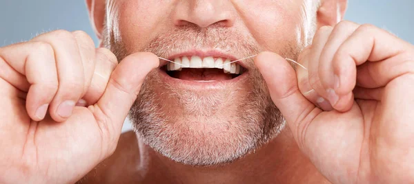 Closeup, floss and man with dental health, cleaning teeth and fresh breath against grey studio background. Male, gentleman and string for oral hygiene, wellness and morning routine for mouth grooming.