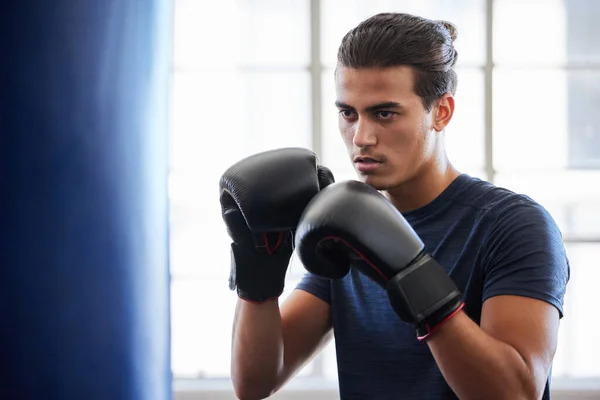 Man, boxing and fitness in gym exercise for power, performance and cardio against a window background. Boxer, fighter and athletic male training on punching bag at sports center, serious and tough.