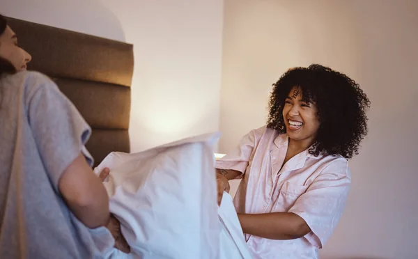 Women, laughing or pillow fight in house, home or hotel bedroom in fun game, energy activity or sleepover challenge. Smile, happy or play fighting friends and linen product, bedding or bonding comedy.