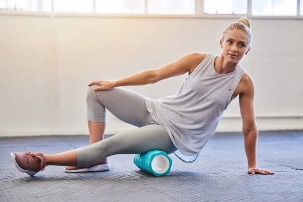 Fitness, physiotherapy and massage, woman with foam roller on floor for leg tension and support in yoga workout at gym. Health, pilates and massaging for sports physio, girl on ground rolling muscle