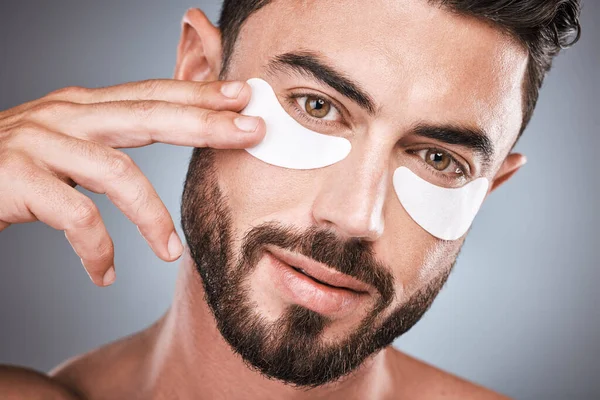Face, skincare and man with eye patches in studio isolated on a gray background for wellness. Portrait, dermatology and male model with cosmetics, facial treatment or mask product for healthy skin