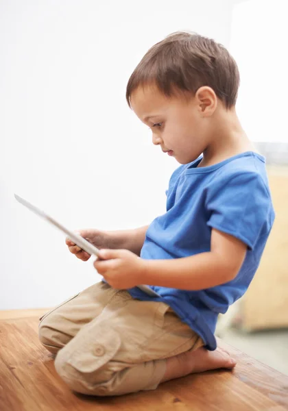 Learning about technology. Sideways shot of a young boy sitting on a table playing with a digital tablet