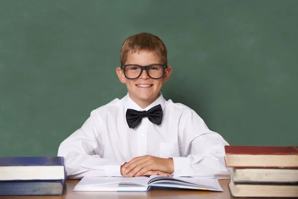Ask me anything. A happy young schoolboy with a bow-tie smiling at the camera in front of a blackboard