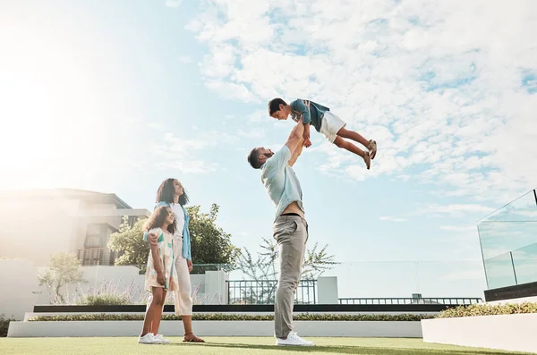 Family, sky and real estate with a man lifting his son outdoor while bonding as a new homeowner group. Kids, love or summer with parents and children standing outside in the garden of a home property.