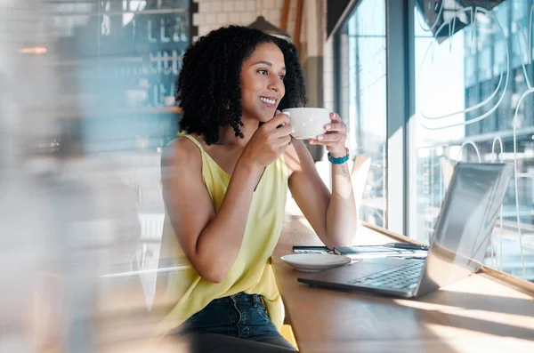 Window, laptop and coffee shop with a black woman blogger drinking a beverage during remote work. Internet cafe, freelance and startup with an attractive young female working in a restaurant.