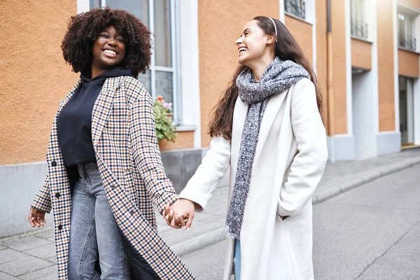 Woman, friends and holding hands with smile in the city for friendship, travel or laughing for fun journey together. Happy women walking, touching hand and smiling for funny outdoor traveling in town.