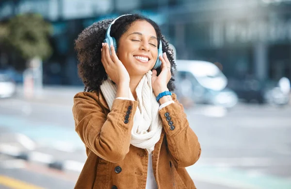 Black woman, music and headphones while happy in city for travel, motivation and mindset. Young person on urban street with radio and sound while listening and streaming podcast or audio outdoor.