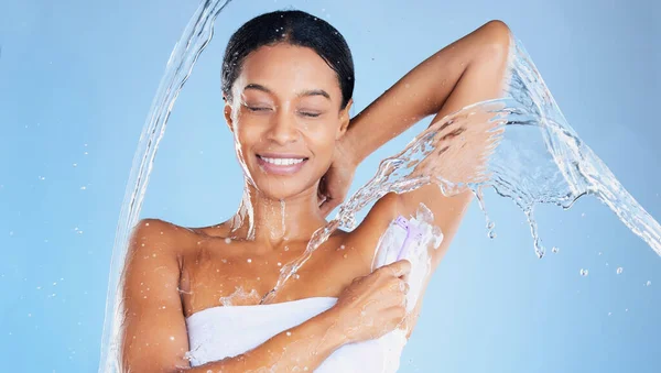 Black woman, water splash or shaving underarms on blue background in relax grooming, body hair removal or healthcare wellness. Beauty model, happy or wet in armpit razor cream for skincare cleaning.