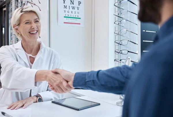 Senior doctor, handshake or man consulting for eyesight advice at optometrist or ophthalmologist with medical aid. Happy customer shaking hands with a trusted optician after checking vision health.