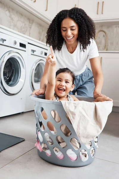 Mom, laundry and girl kid in basket by washing machine for cleaning, bonding or comic time in house. Crazy fun, mother and daughter with happiness, love and playing in family home with smile on face.