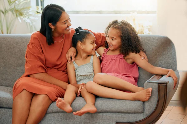 A happy mixed race family of three relaxing in the lounge and sitting on the couch together. Loving black single parent bonding with her daughters while relaxing on a sofa at home.