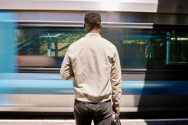Black businessman travelling alone. Rear View of a african american businessman waiting for a train at a railway station during his commute at a train station.