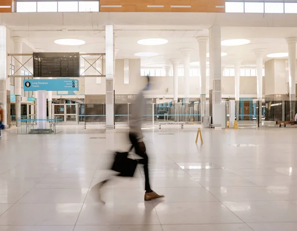 Blurred businessman travelling alone and walking in a train station while wearing a mask for protection against coronavirus. Young black male on his way to work in a station in the morning.