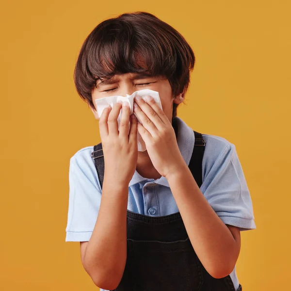 One mixed race Asian boy blowing his nose while looking sick and posing against an orange copyspace background. Cute Asian kid with a runny nose and an allergy.