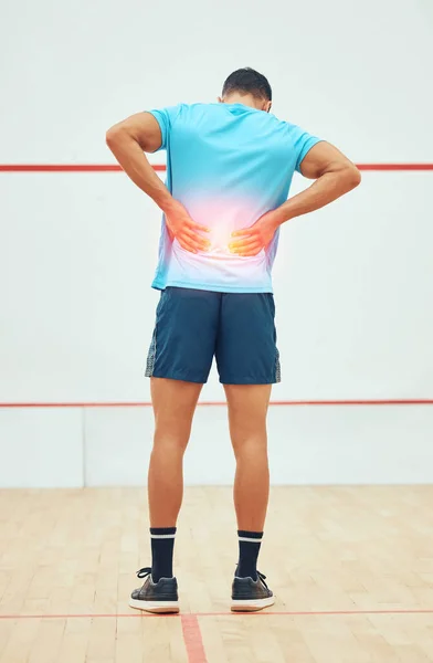 Full length rearview of unknown squash player suffering from backache during court game. Fit active mixed race athlete standing and feeling pain. Cgi and special effects on sports injury after playin.