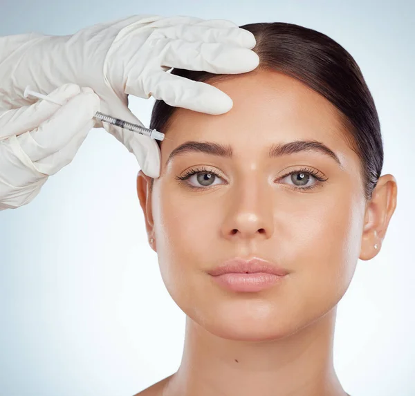 Closeup portrait of woman getting facial fillers or botox. Young caucasian model isolated against a grey studio background with copyspace. Dermatologist injecting patient during cosmetic procedure.