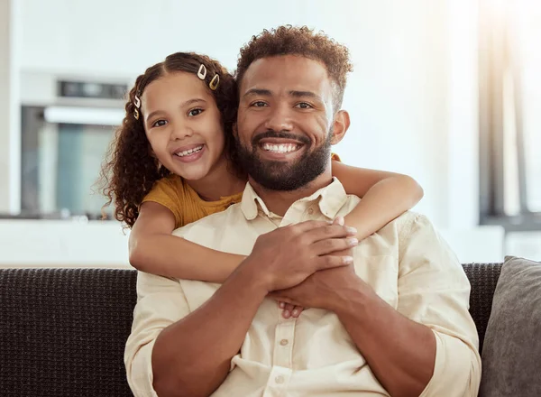 Portrait of mixed race single father and daughter hugging in home living room. Smiling hispanic girl embracing and bonding with single parent in lounge. Happy man and child sitting together on weeken.