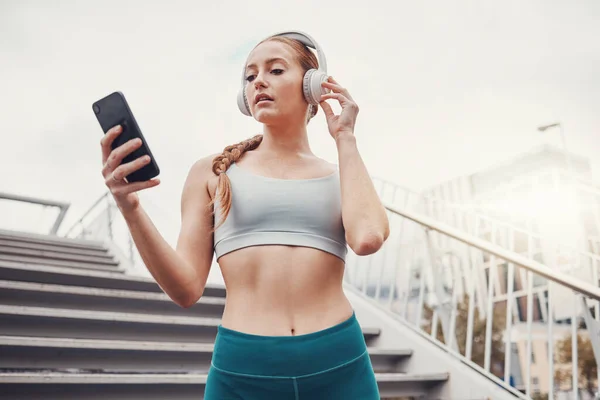 Woman, runner and phone with headphones for music, radio and web texting on chat app by stairs. Gen z girl, urban workout and fitness with smartphone for networking, social media and internet in city.