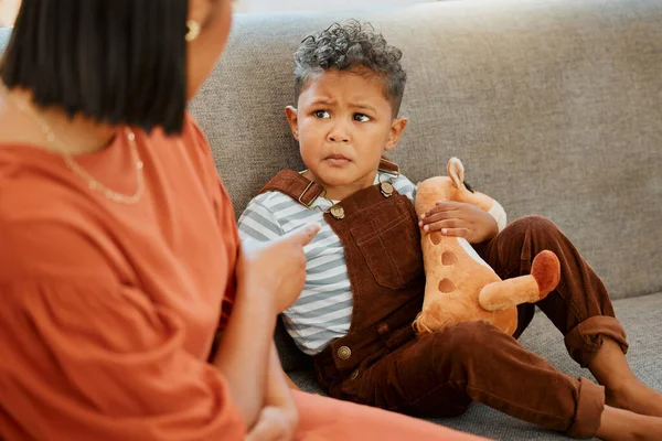A single parent putting her son in timeout for his bad behaviour. Closeup of a mixed race single parent being a bully to her depressed son while he holds a teddybear for comfort at home.
