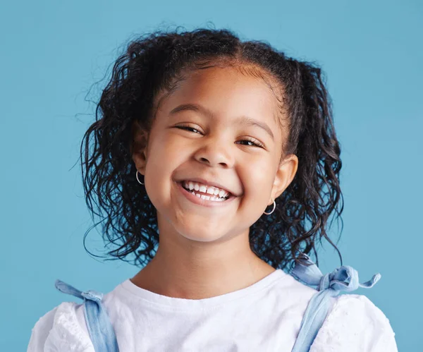Close up head shot with smiling little brown haired girl looking up. Happy kid with good healthy teeth for dental on blue background.
