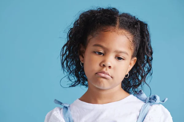 Offended little hispanic girl looking sad and upset while posing against a blue studio background. Unhappy preschooler looking down.