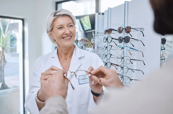 Glasses, retail store and sale of a senior eye doctor holding a frame to help customer shopping. Happy optometrist, shop wellness and service of an elderly eyes expert with eyeglasses vision check.