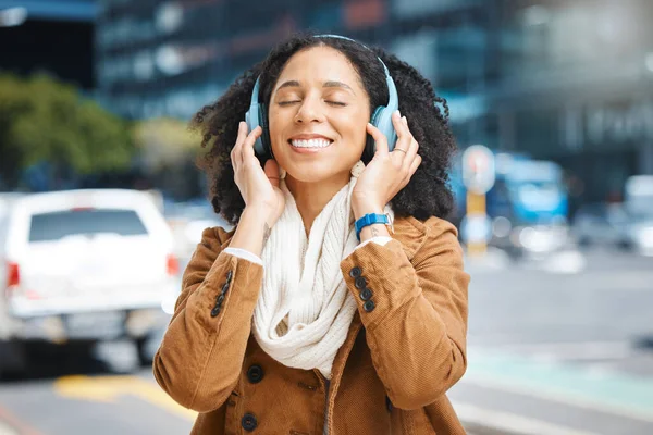 Black woman with headphones for listening to music in city for travel, motivation and happy mindset. Young person on an urban street with buildings background while streaming podcast or audio outdoor.