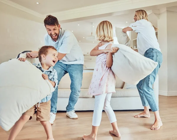 Playful parents with little kids pillow fighting in their living room. Adorable caucasian children enjoying free time with their mother and father. Happy family standing and play fighting at home.