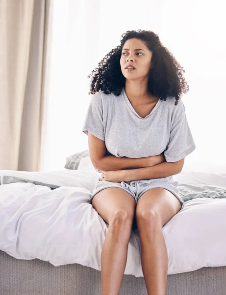 Black woman, sick and stomach ache on house bed, home or bedroom in period pain, menstruation cramps or ibs crisis. Hurt person, injury and abdomen tummy in healthcare emergency or appendicitis risk.