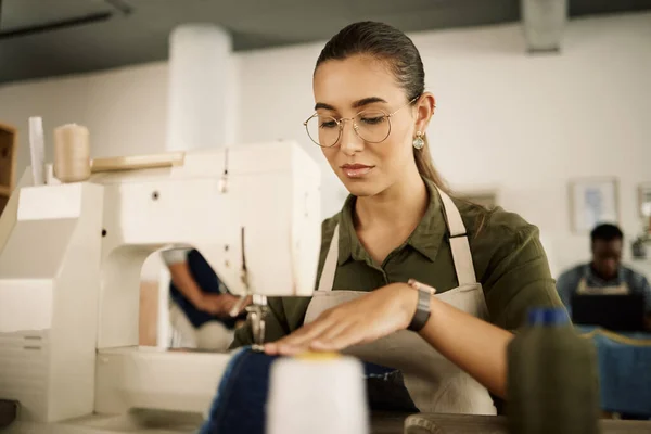 Mixed race designer sewing on a machine. Young fashion designer stitching denim fabric. Serious tailor working in her studio. Creative entrepreneur sewing material on sewing machine.