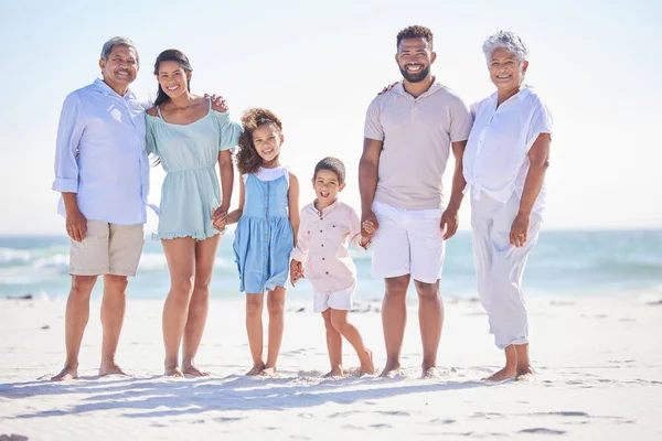 Multi generation family on holding hands while standing on the beach together. Mixed race family with two children, two parents and grandparents spending time together by the sea.