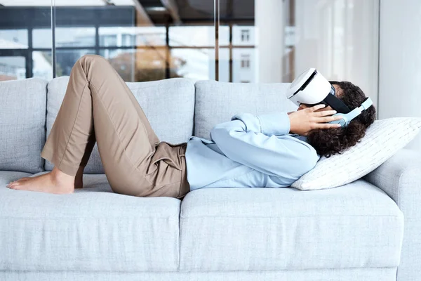 Virtual reality, metaverse and 3D gaming with a black woman on a sofa in the living room of her home. AI, VR and simulation with a female gamer using a headset to access cyberspace for a video game.