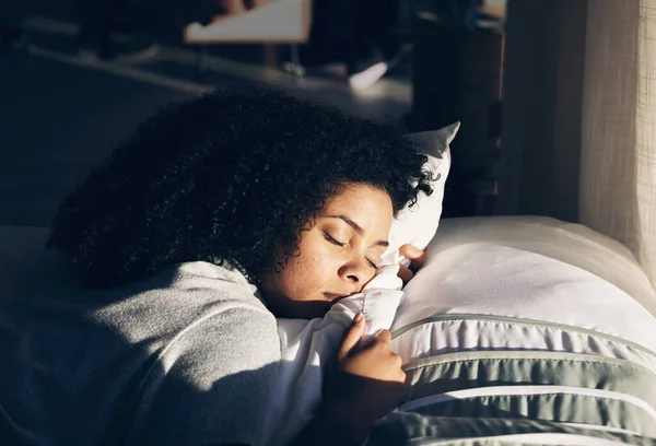 Black woman, sleeping in bed for peace, quiet and rest or relax in home bedroom. Person with pillow to dream or for calm sleep with sunlight for health and wellness in apartment or hotel.