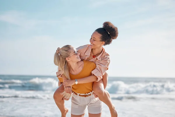 Piggyback, ocean and happy couple of friends for lgbtq, lesbian or love and freedom on summer vacation together. Blue sky, beach and diversity women on date, fun support or excited valentines holiday.