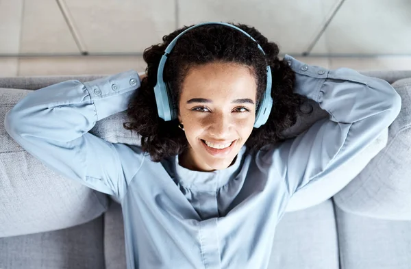 Top view, portrait and woman on sofa, headphones and relax for break, peace and smile with joy. Female, lady and headset music, streaming and listen to podcast for happiness, cheerful and peaceful.