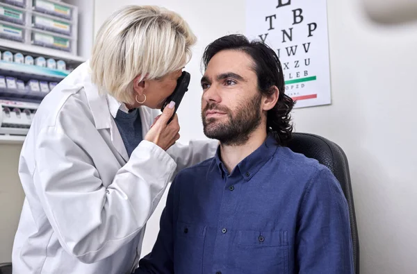 Doctor with a man in a vision test or eye exam for eyesight by doctor, optometrist or ophthalmologist with medical aid. Patient or client with a helpful senior optician to see or check glaucoma.