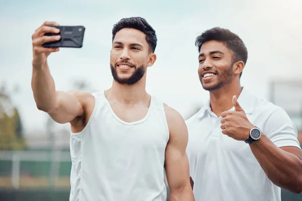 Portrait of two smiling ethnic tennis players taking selfie on cellphone after playing court game. Happy ethnic athletes team bonding, taking picture on phone. Friends play sports for healthy fitness.