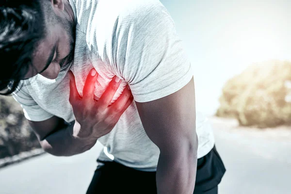 Closeup fit mixed race man holding his chest in pain while exercising outdoors. Unrecognizable male athlete struggling to breath, having a heart attack or going into cardiac arrest, highlighted by cg.
