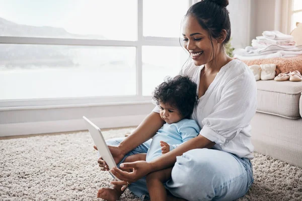 Raising children is different in the modern era. an attractive young woman sitting on the living room floor with her daughter and using a digital tablet