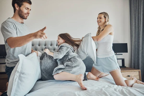 Family in pillow fight, happiness and fun together at home, parents and child in bedroom, playful and bonding. .Man, woman and girl play game, funny and crazy with energy and love with quality time.