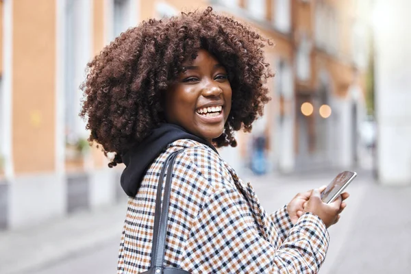 Phone, happy and portrait of a black woman in the city networking on social media, mobile app or internet. Happiness, smile and African female typing a message on a cellphone while walking in town