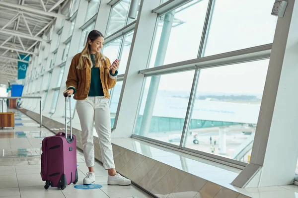 Luggage, travel and woman with phone at airport for social media, web scrolling or internet browsing. Suitcase, mobile and happy female on smartphone for networking while waiting for flight departure.