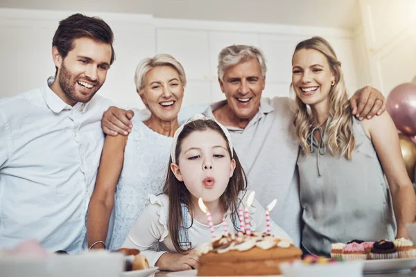 Cake, birthday and big family with girl blowing out candles for wish, party or celebration event. Love, food and kid with happy father, mother and grandparents celebrating special day in home kitchen.