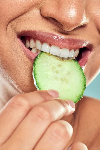 The inside matters just as much as the outside. a woman biting into a slice of cucumber against a studio background
