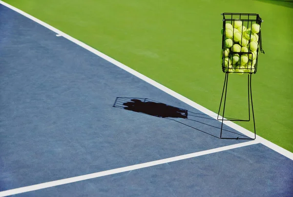 Tennis, sport balls and basket of sports equipment on a training court outdoor with no people. Exercise, fitness and workout equipment shadow for match of game competition on turf ground in summer.