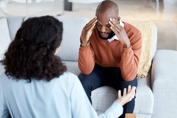 Black man, mental health and counseling with woman psychologist, stress headache and depression with help. Consultation, doctor with patient and conversation about anxiety problem, sad and depressed.