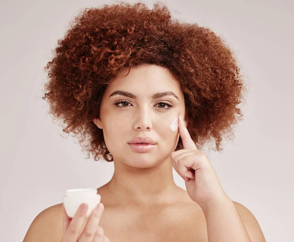 Skincare, beauty and portrait of black woman with lotion on face, afro and advertising luxury skin product promotion. Dermatology, cosmetics and facial, model with jar isolated on studio background