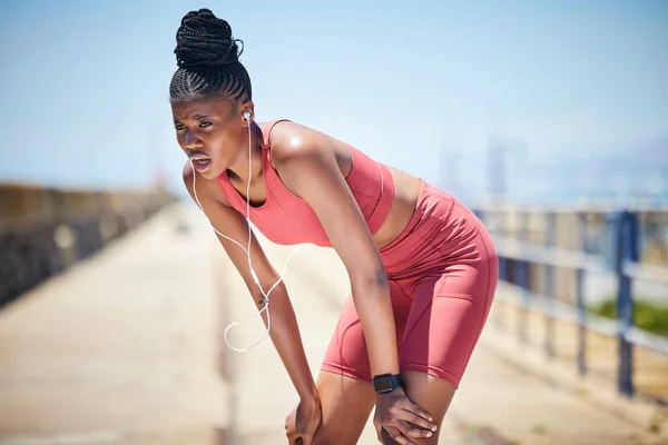 Tired black woman breathing outdoor for fitness, healthy target and body fatigue. Female athlete, break and breathe for sports workout, running exercise and music earphones of city training challenge.
